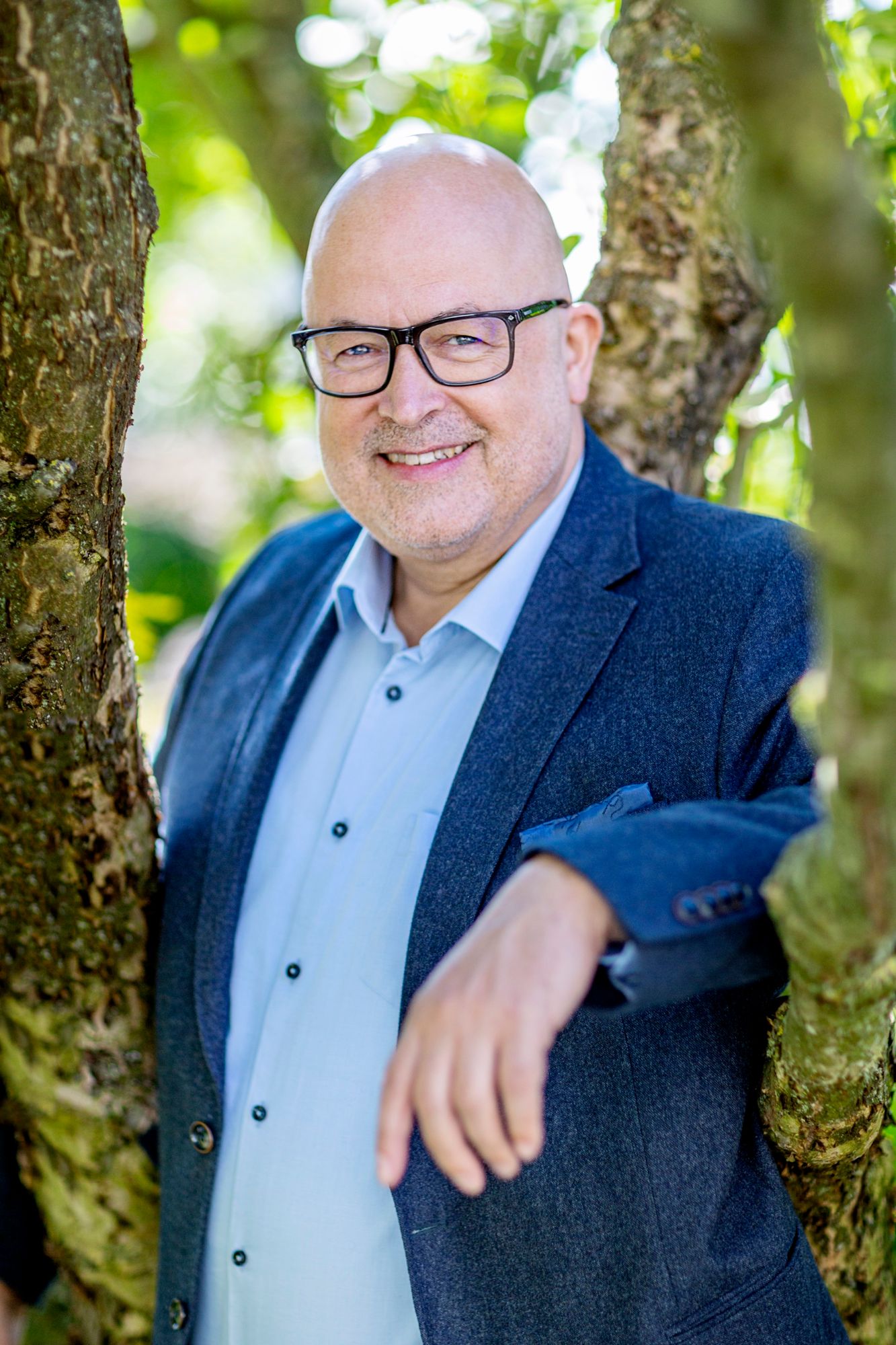 Norbert Peter, lächelnd an einen Baum gelehnt